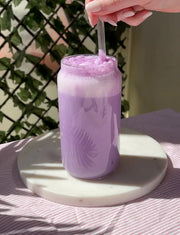 Ube latte glacé à la poudre d'ube mélangé avec une paille en verre, couleur violet lavande onctueuse dans un grand verre