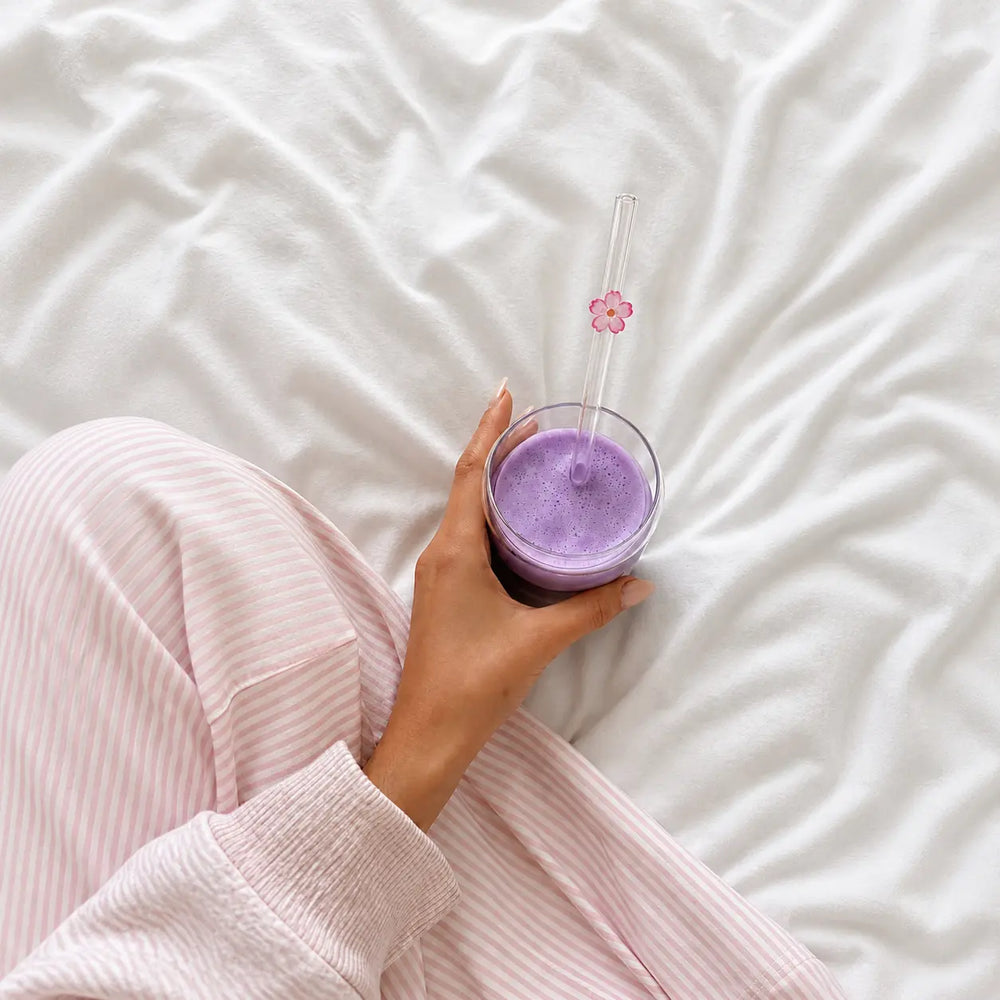 Ube latte à la poudre d'ube tenu à la main dans un verre bubble, avec une épaisse mousse de lait blanche et paille en verre