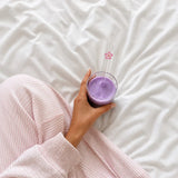 Ube latte à la poudre d'ube tenu à la main dans un verre bubble, avec une épaisse mousse de lait blanche et paille en verre