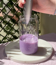 Préparation d'un ube latte maison à la poudre d'ube avec un mousseur électrique, mélange violet dans un verre sur plateau en marbre