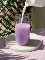 Préparation d'un ube latte glacé : versement de lait sur la poudre d'ube dans un grand verre, couleur violet lavande